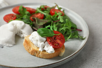 Delicious burrata cheese with tomatoes, arugula and toast on grey table, closeup