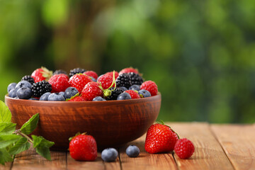 Bowl with different fresh ripe berries on wooden table outdoors, space for text