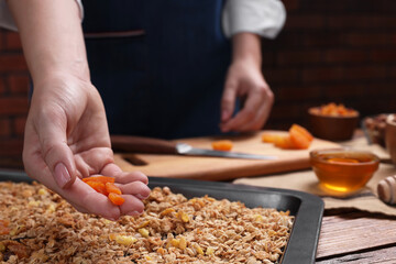 Making granola. Woman with dry apricots at table in kitchen, closeup