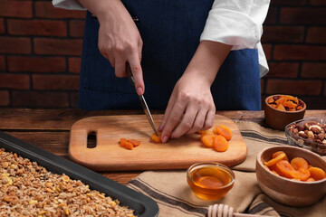 Making granola. Woman cutting dry apricots at wooden table, closeup