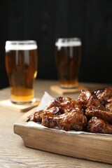 Tasty chicken wings and glasses of beer on wooden table. Delicious snack