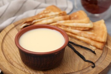 Tasty condensed milk and crepes on wooden board, closeup