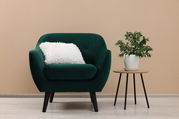 Stylish armchair and side table with plant near beige wall indoors