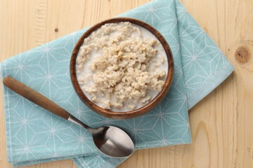 Tasty boiled oatmeal in bowl and spoon on wooden table, top view