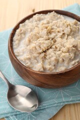 Tasty boiled oatmeal in bowl and spoon on wooden table, closeup
