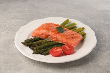 Tasty grilled salmon with tomatoes and asparagus on grey table