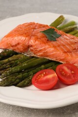 Tasty grilled salmon with tomatoes and asparagus on grey table, closeup