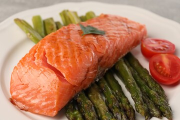 Tasty grilled salmon with tomatoes and asparagus on plate, closeup