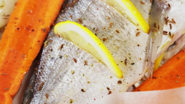 Fresh uncooked fish dorado with lemon, cumin seeds and carrot on parchment paper. Top view