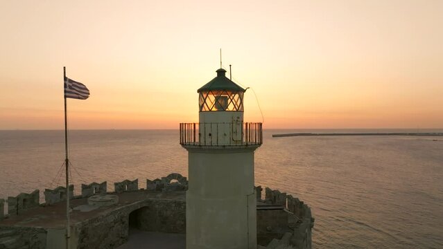 Sunrise over Medieval fortification lighthouse and Greek flag in the island of Rhodes, Greece