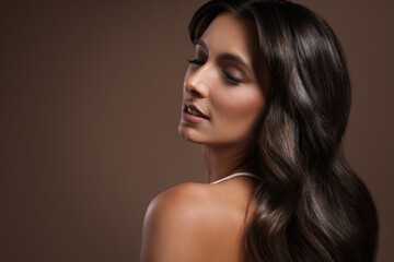 Obraz premium Gorgeous woman with shiny wavy hair on brown background, space for text. Professional hairstyling