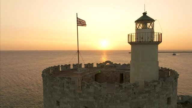 Sunrise over Medieval fortification lighthouse and Greek flag in the island of Rhodes, Greece
