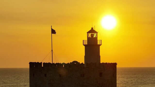 Sunrise over Medieval fortification lighthouse and Greek flag in the island of Rhodes, Greece