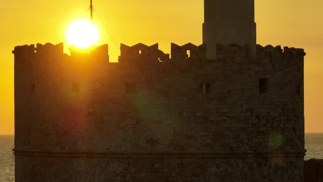 Sunrise over Medieval fortification lighthouse and Greek flag in the island of Rhodes, Greece