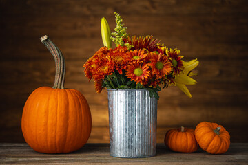 Autumn or Fall still life. Pumpkin and bouquet of red, yellow, orange flowers in a metal bucket on natural wooden table and background. Happy Thanksgiving Day. Autumn mood. High resolution photo. © Anna