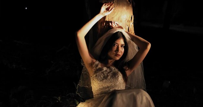 Scary Asian girl in Halloween bride dress costume in the dark forest.