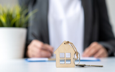 Businesswoman signing contract on background. Keychain in shape of miniature house and key close...