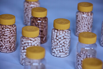 Dietary supplement manufacturing different color capsules filled in clear bottles on blue background