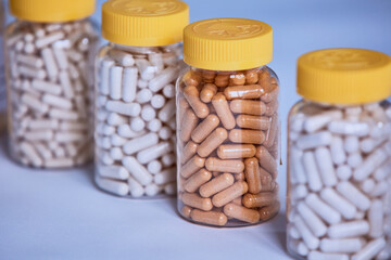 Dietary supplement manufacturing different color capsules filled in clear bottles on blue background