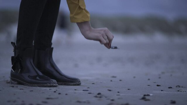 A woman in rubber boots picking up something from the beach