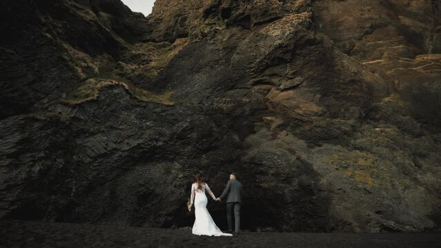 Brave married couple, wearing wedding outfits, discovering majesty of twisting basalt columns with a mysterious cave, located on south coast of Iceland. High quality 4k footage