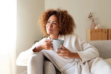 Foto op Plexiglas Pensive multiracial woman relaxing at home, sitting on the sofa drinking tea. © Daniel