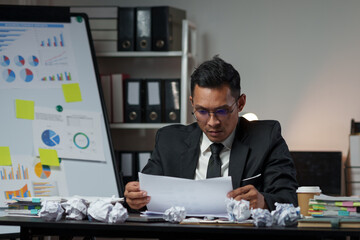 Fototapeta na wymiar Technology concept, dark-skinned Asian businessman wearing glasses sits and works with a laptop computer. Stack of documents and cell phones for contacting work within the office.
