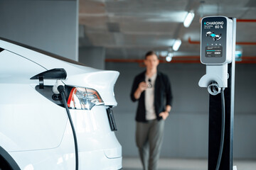 Young man travel with EV electric car to shopping center parking lot charging in downtown city...