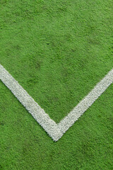 vertical image of the corner of a synthetic grass soccer field, where the white line called the corner quadrant forms a V, a slightly worn and dirty field