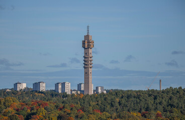 Obraz premium Tele tower in a colorful autumn forest and skyscraper apartment houses in background, a sunny autumn day in Stockholm