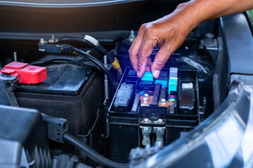 A mechanic is opening the cover of a car's electrical system control box.