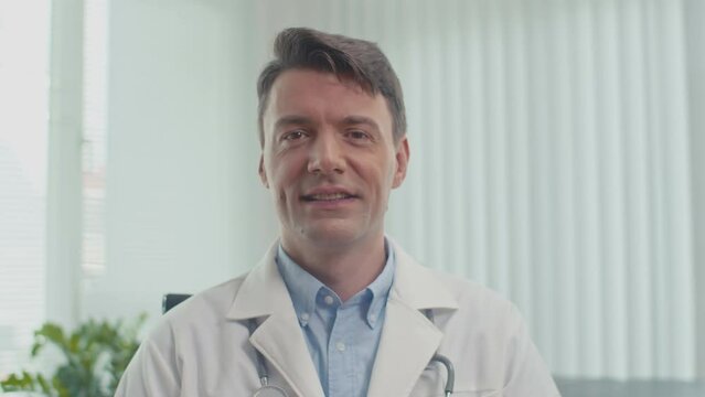 Portrait of positive doctor in labcoat sitting at workplace and looking at camera