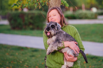 Mature woman holding her schnauzer dog on the arm in the summer park.