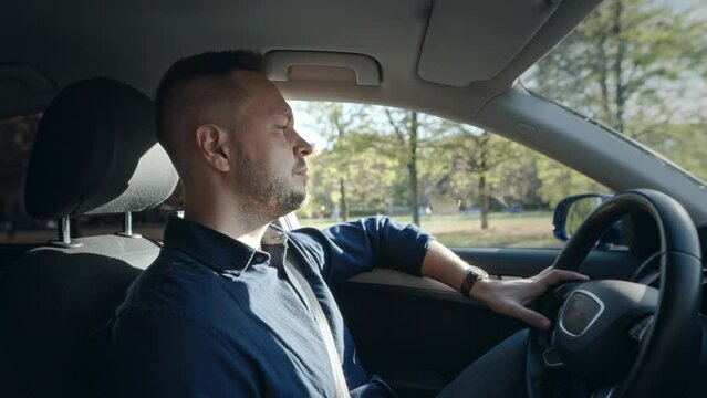 An adult and serious man is driving a car. The driver is focused on the road and controlling the car.