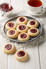 Thumbprint Christmas cookies filled with raspberry jam closeup on the plate served with tea on the white wooden table. Vertical