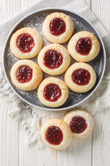Classic thumbprint cookies are made with a simple sugar cookie dough and then indented and filled with Raspberry jam closeup on the plate on the white wooden table. Vertical top view from above