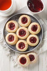 Thumbprint Christmas cookies filled with raspberry jam closeup on the plate served with tea on the white wooden table. Vertical top view from above