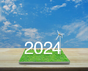 2024 white text with wind turbine on green grass on open book on wooden table over blue sky with white clouds, Happy new year 2024 ecological cover concept