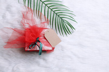 Wrapped gift box with blank price tag mockup and palm leaf on white fur rug. Boxing day design...