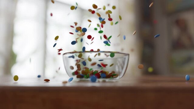 Side view of Chocolate Lentils Falling into a glass Bowl on a wooden table