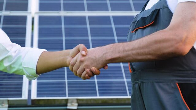 Two engineers, Indian manager and senior subordinate shaking hands after discussion on background of photovoltaic solar panels, close up