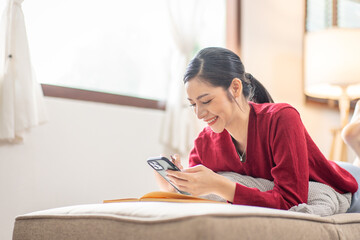 Naklejka premium Happy relaxed young woman sitting on couch using cell phone, smiling lady laughing holding smartphone, looking at cellphone enjoying doing online ecommerce shopping in mobile apps or watching videos.