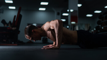 Muscular shirtless man doing push ups in the gym. 