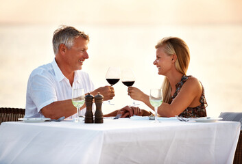 Beach, dinner and couple with sunset, cheers and romance with anniversary, marriage and seaside holiday. Travelling, romantic meal and man with woman, ocean and bonding together with tropical island