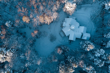 Aerial view of an old manor house hidden among a fabulous snow-covered forest in winter. The...