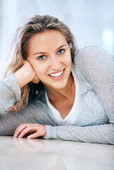 Woman, portrait and floor lying smile in home for cheerful friendly, calm or feminine look. Female person, happy face and hand on ground for attractive, lazy weekend joy or positive relax in Canada