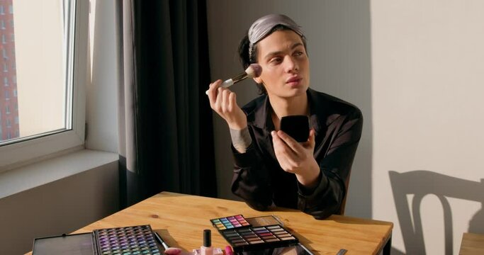 transgenes queer man puts on make up Beauty routine sitting at table. metrosexual applying powder with brush, preparing for date Slow motion Gay pride day parade Non-binary person applying makeup