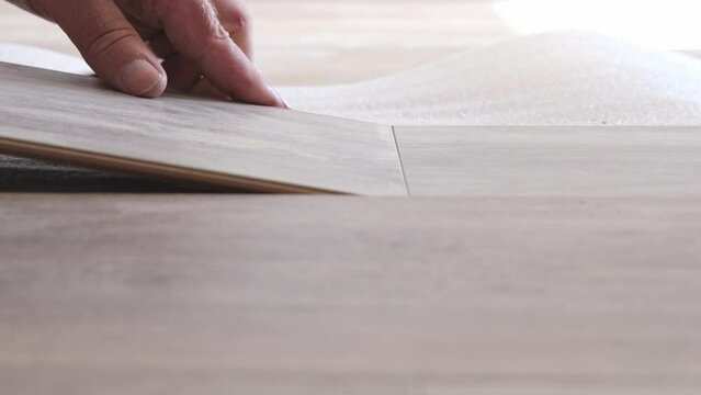 A man changes the floor in the apartment, lays the floor of a wooden gray laminate in the house. Close-up on a man's hands