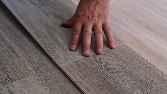 A man changes the floor in the apartment, lays the floor of a wooden gray laminate in the house. Close-up on a man's hands