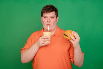Portrait of a fat guy eating a big hamburger and drinking soda from a glass with a straw, isolated...